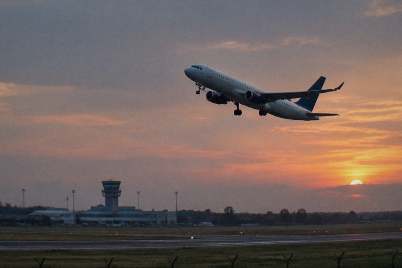 A passenger plane climbing above an airport runway at dusk