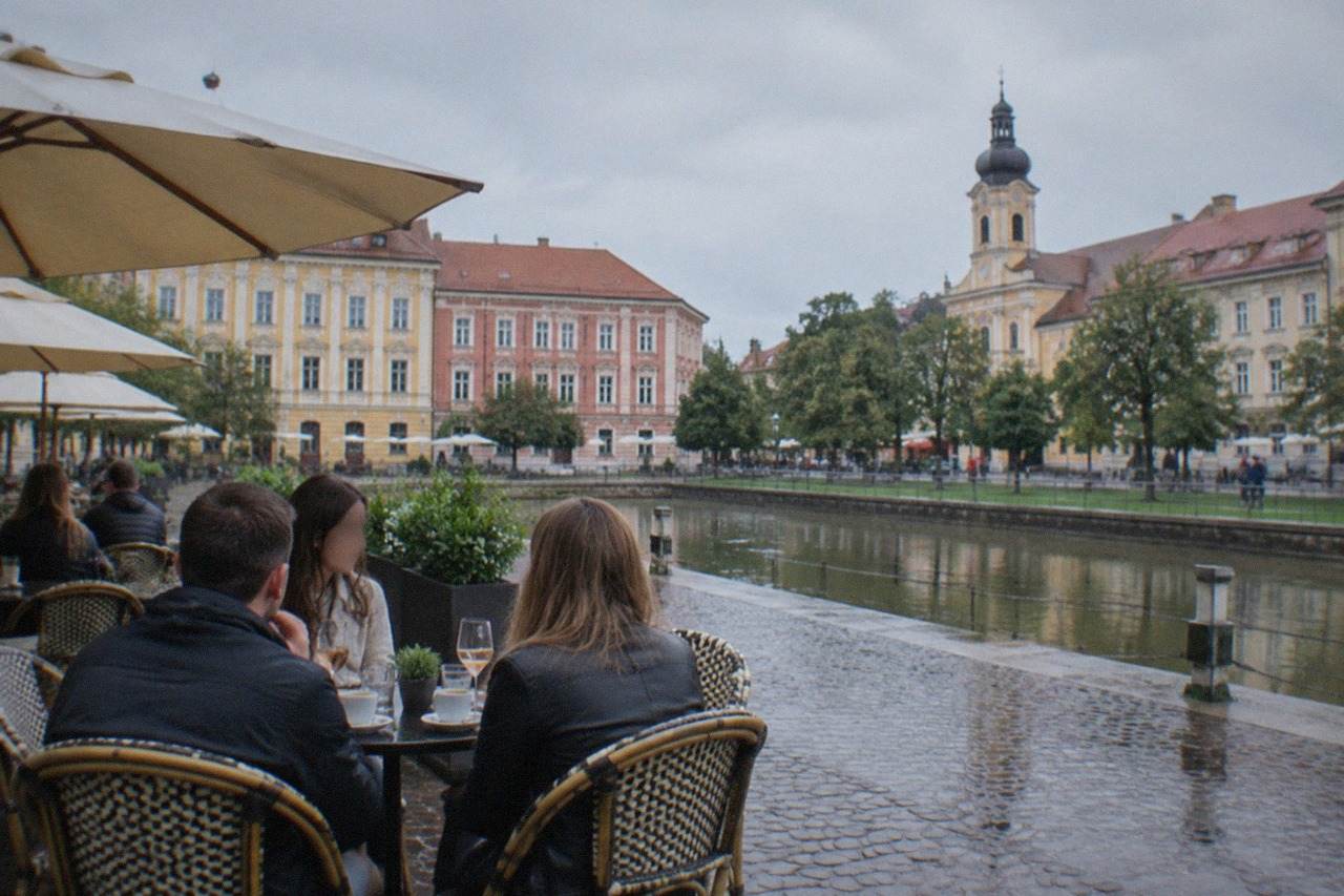 Visitors and locals talking at an outdoor cafe table on a colorful square in Timisoara