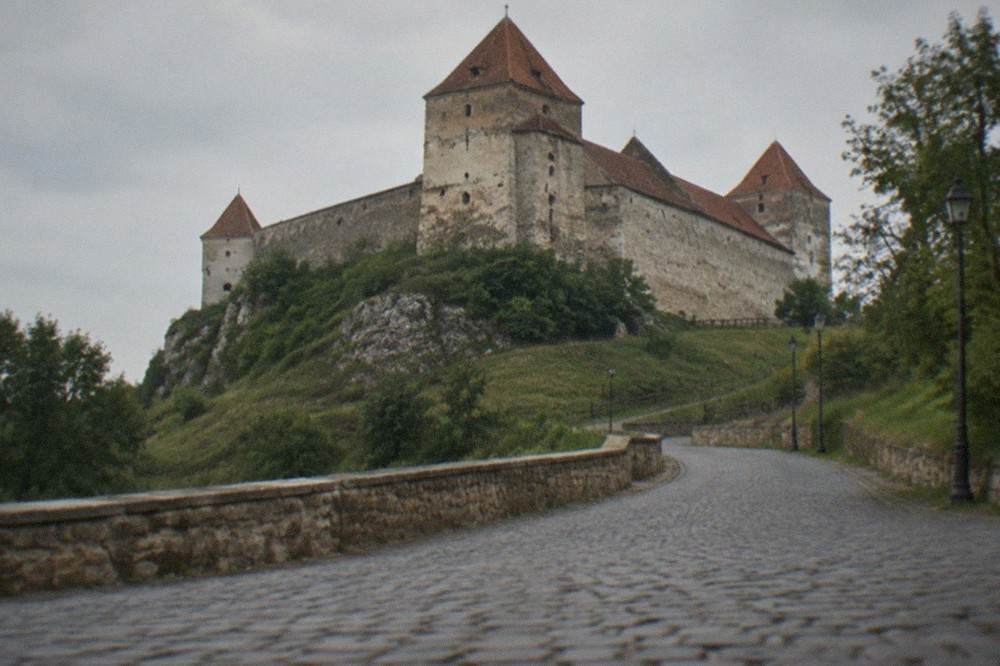 A medieval castle on a hill above a Romanian town, seen from the access road