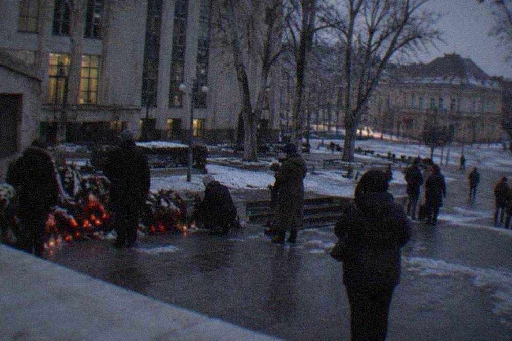 People laying flowers at a monument in a European city square in winter