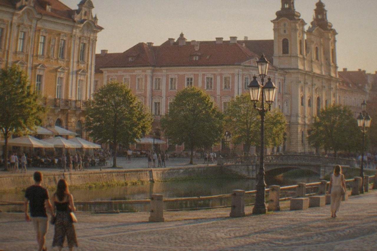 People strolling across a sunny square in central Timisoara lined with colorful baroque buildings