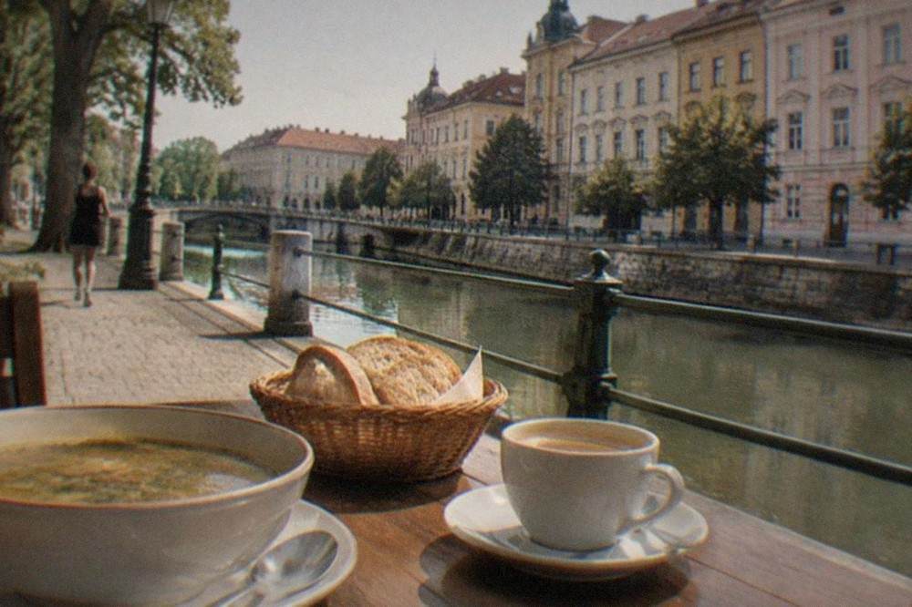 A bowl of sour soup and fresh bread on a wooden restaurant table, with a coffee cup beside it