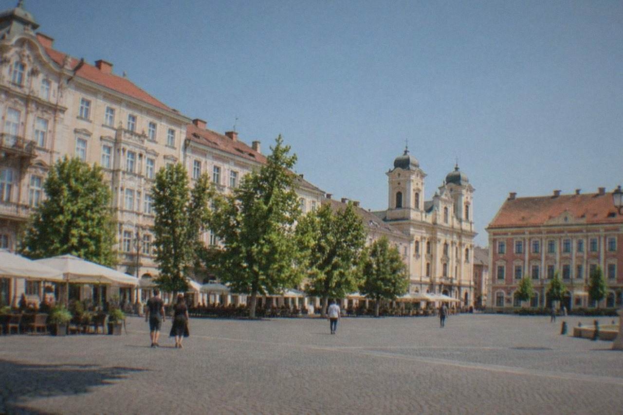 Pastel-colored baroque buildings around a wide square in Timisoara's old town on a sunny day