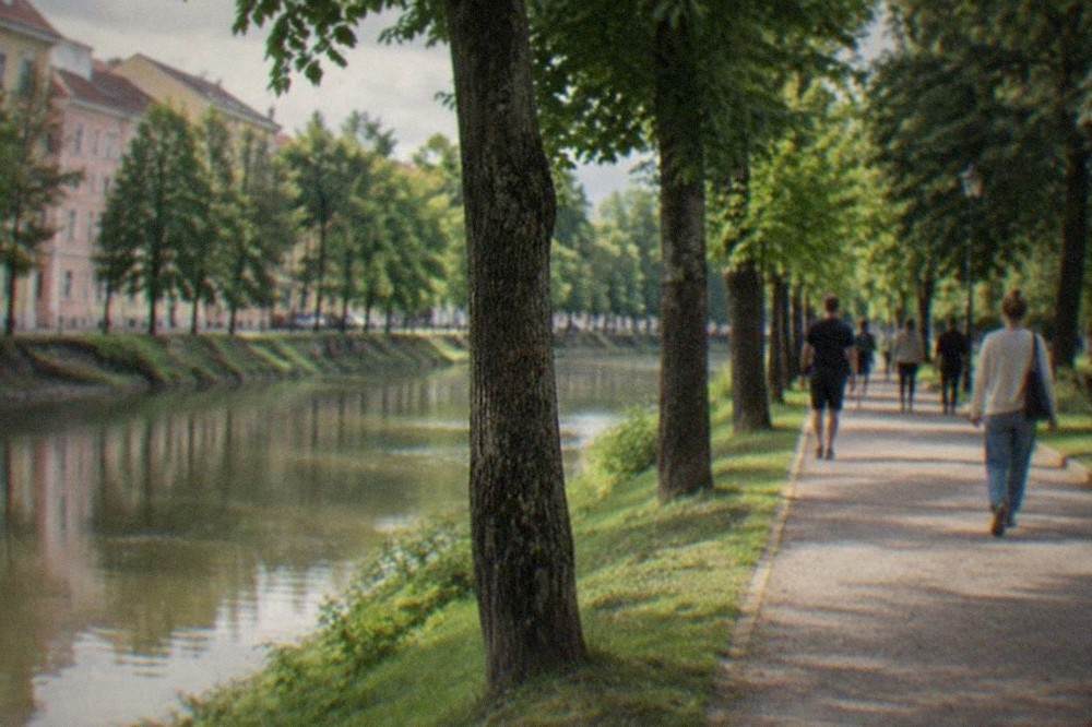 People walking along a tree-lined promenade beside the Bega canal in Timisoara