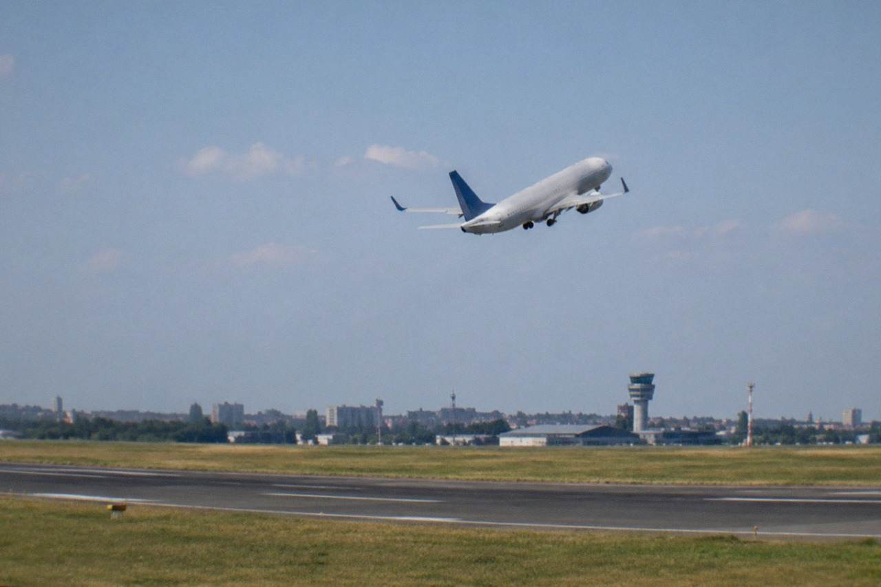 A passenger airplane climbing above an airport runway under a wide afternoon sky