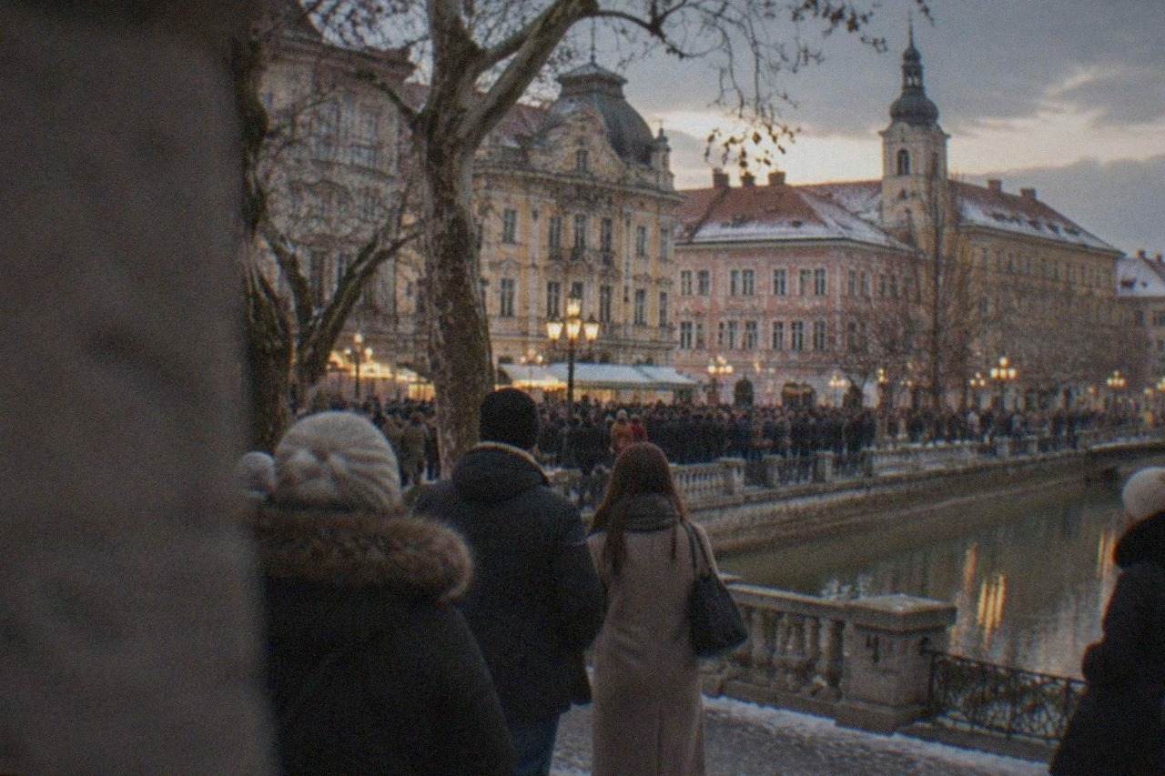 Crowds gathered in a European square at dusk with historic buildings behind them