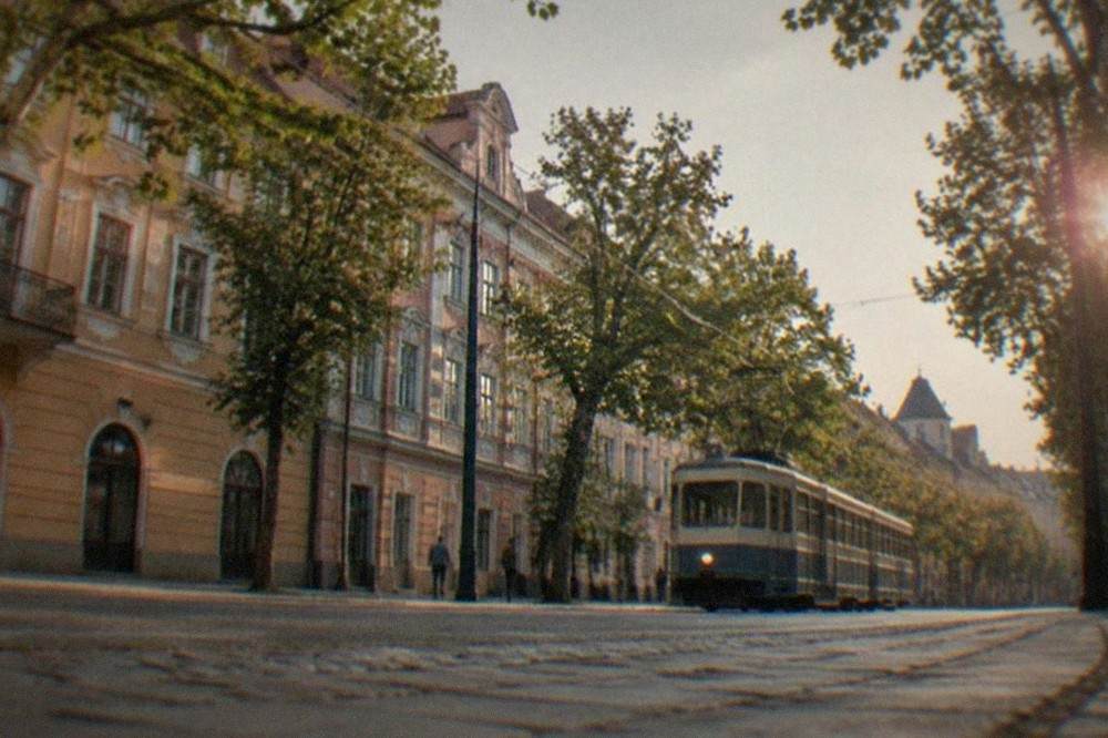 A tram moving along a tree-lined street in Timisoara past pastel-colored facades