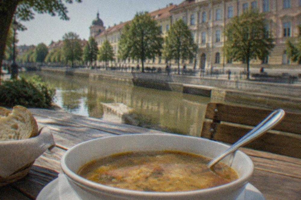 A bowl of sour soup with a spoon and bread on a wooden table