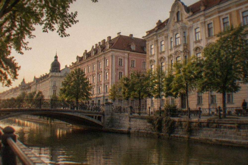 A tree-lined canal promenade with a bridge and historic buildings behind it