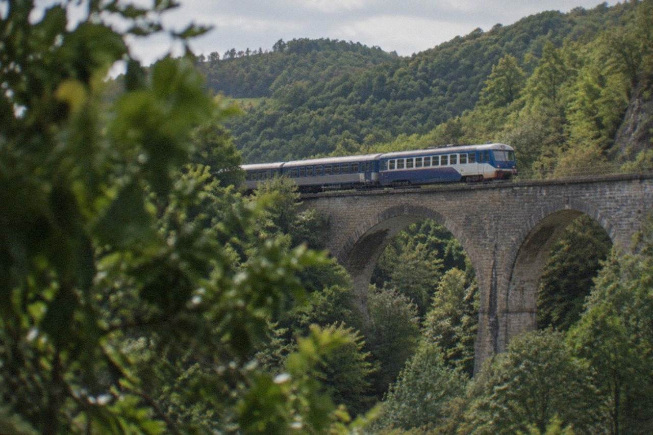 A small passenger train crossing a stone viaduct above a forested valley in the Banat hills of western Romania