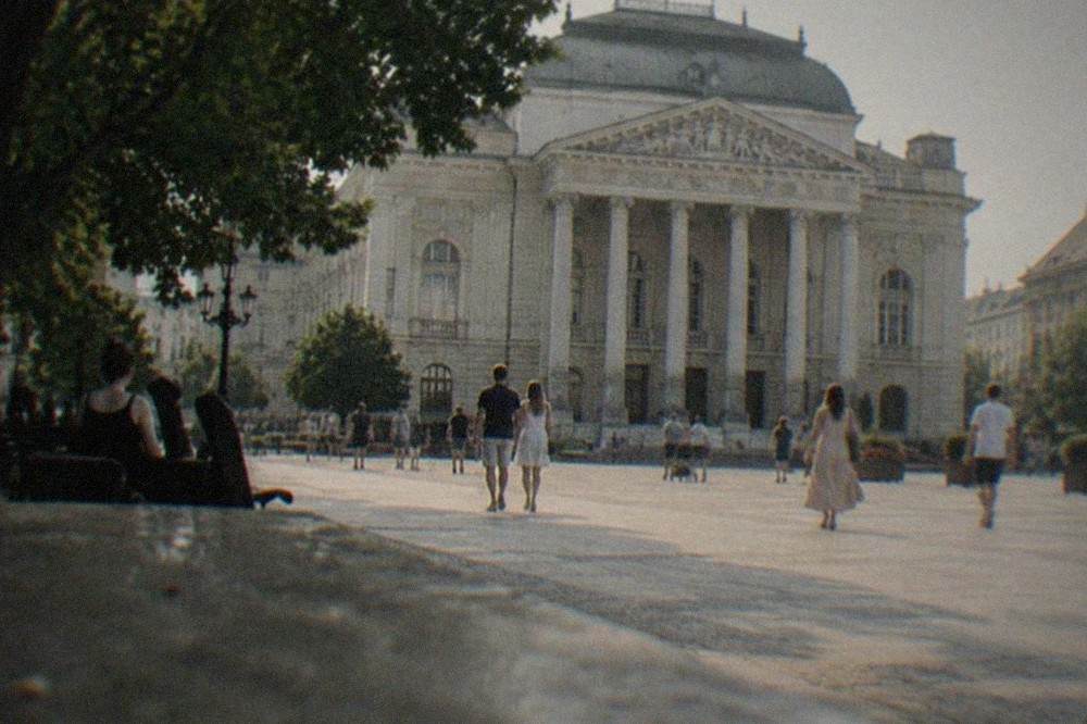 Strollers on a wide square in front of the opera house in central Timisoara on a summer evening