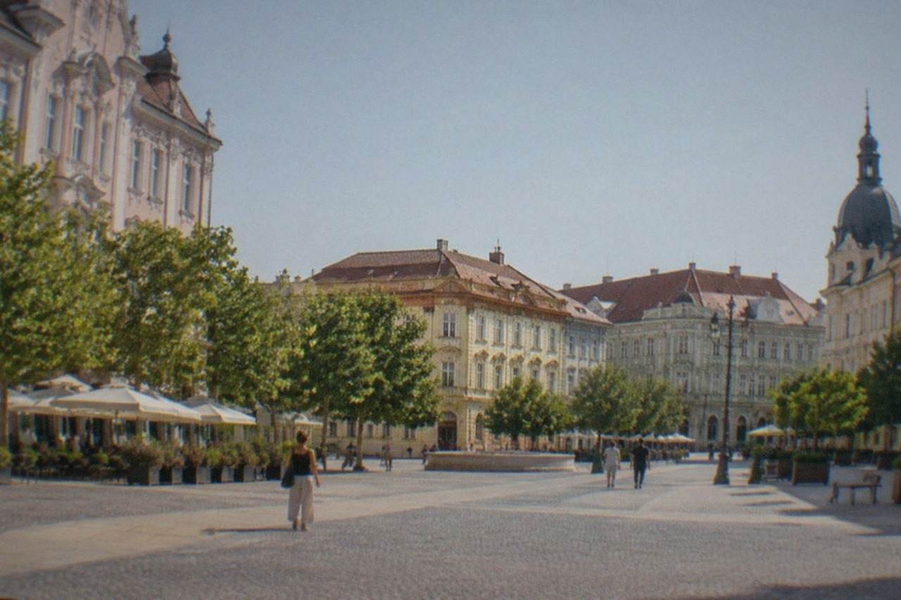 Pastel-colored baroque buildings lining a wide pedestrian square in a European old town on a sunny afternoon