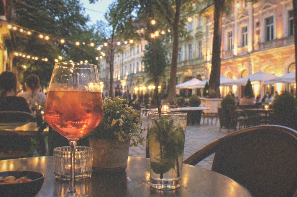 Outdoor cafe tables with drinks under string lights on a pedestrian street at evening