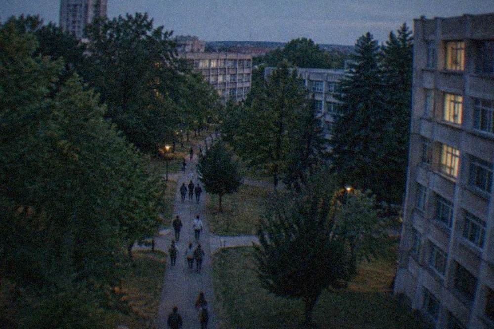 Students walking between faculty buildings on a campus path shaded by mature trees
