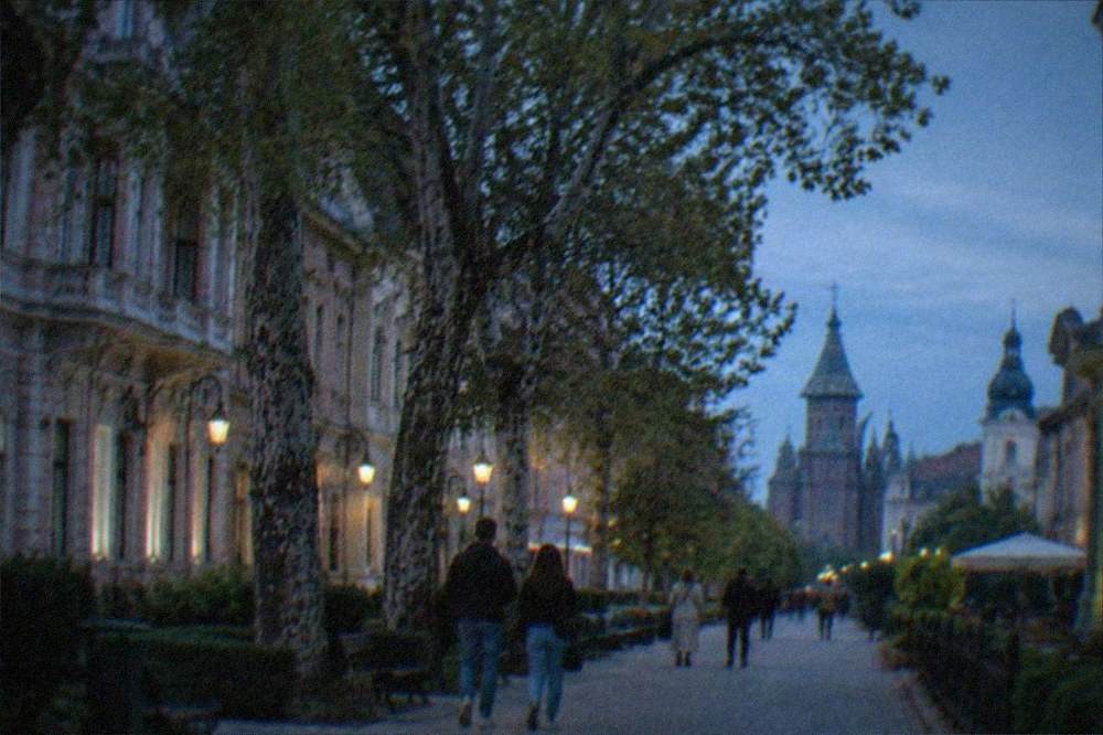 People strolling under plane trees on a quiet residential street in Elisabetin with the old town towers visible in the distance