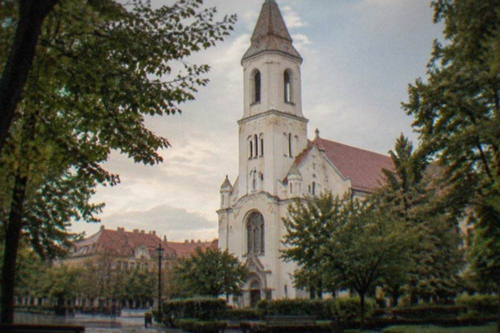 The Millennium Church in Timisoara seen from a tree-lined square with red rooftops behind it