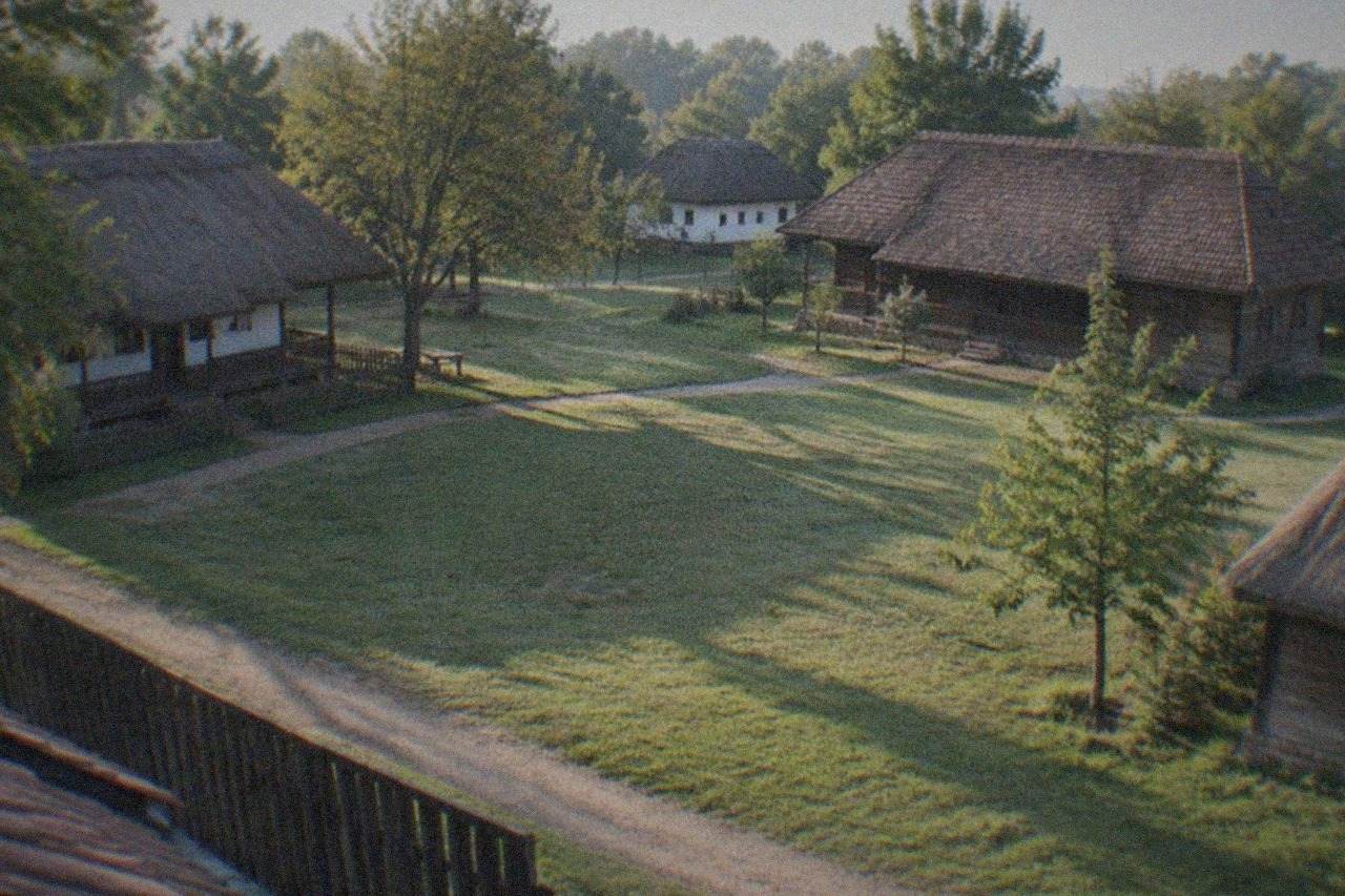 Traditional wooden farmhouses with thatched and tiled roofs arranged around a green lawn at an open-air village museum