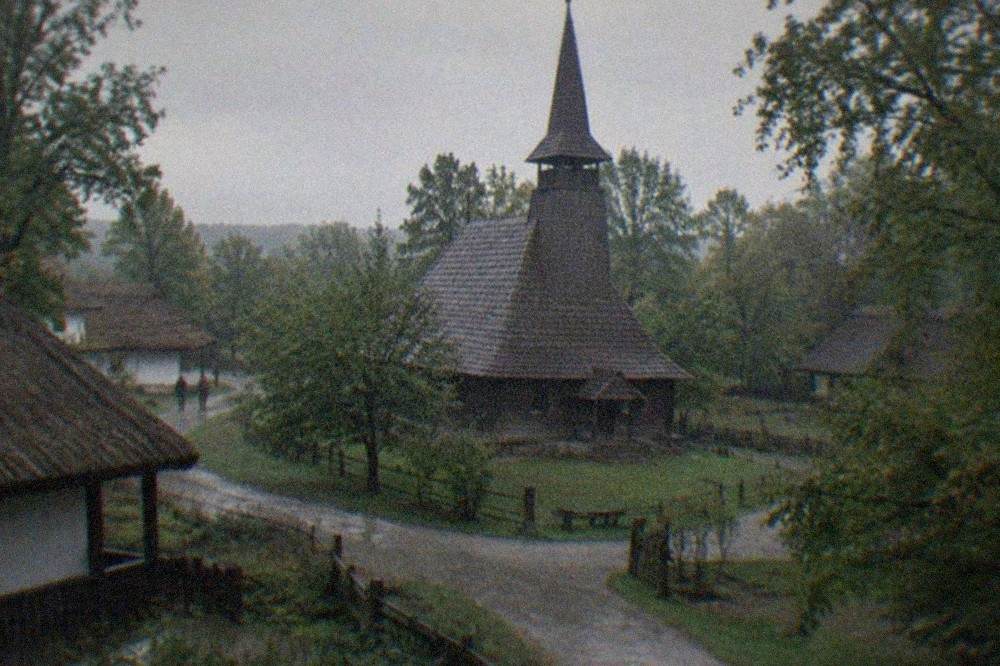A wooden village church with a shingled spire standing among trees at the open-air museum