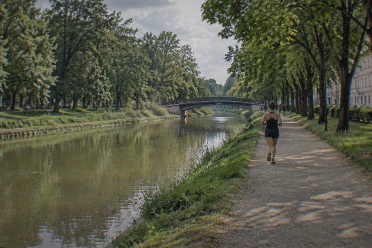 A calm canal crossing a green city park with tree-lined banks and a bridge in the distance