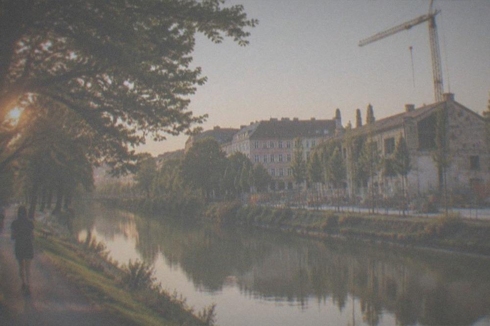 A riverside construction site with new paving, young planted trees and a crane behind an old industrial building