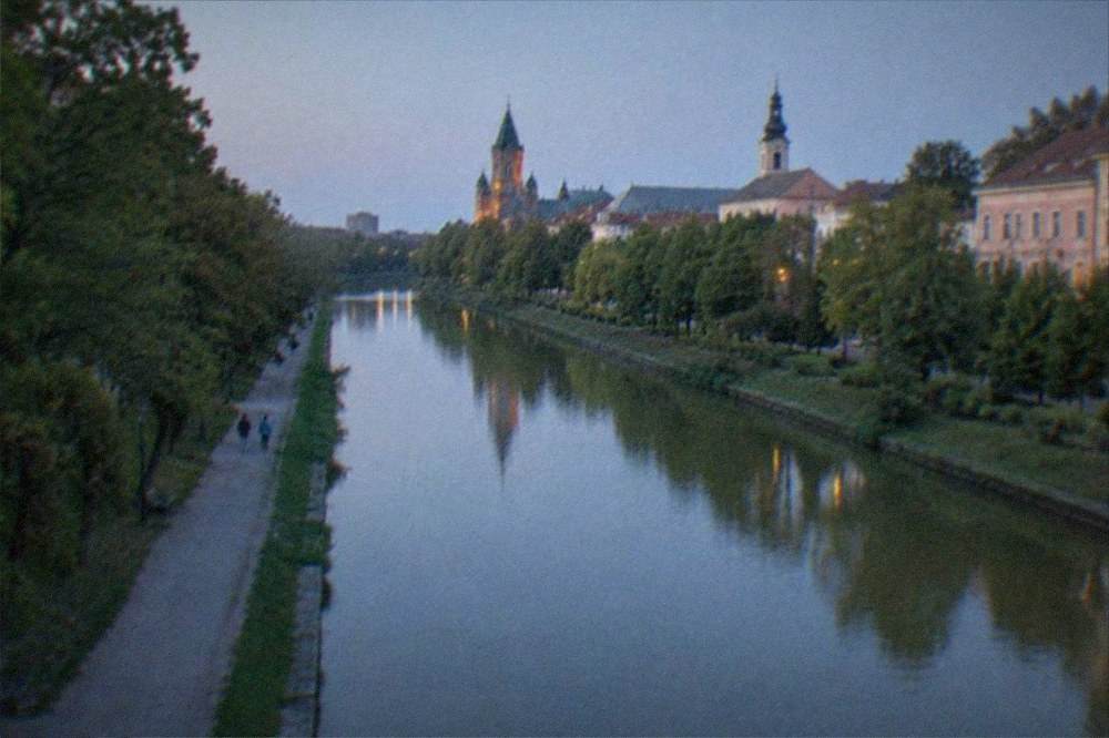 A wide canal view toward a historic city skyline with church towers and rooftops under a clear sky