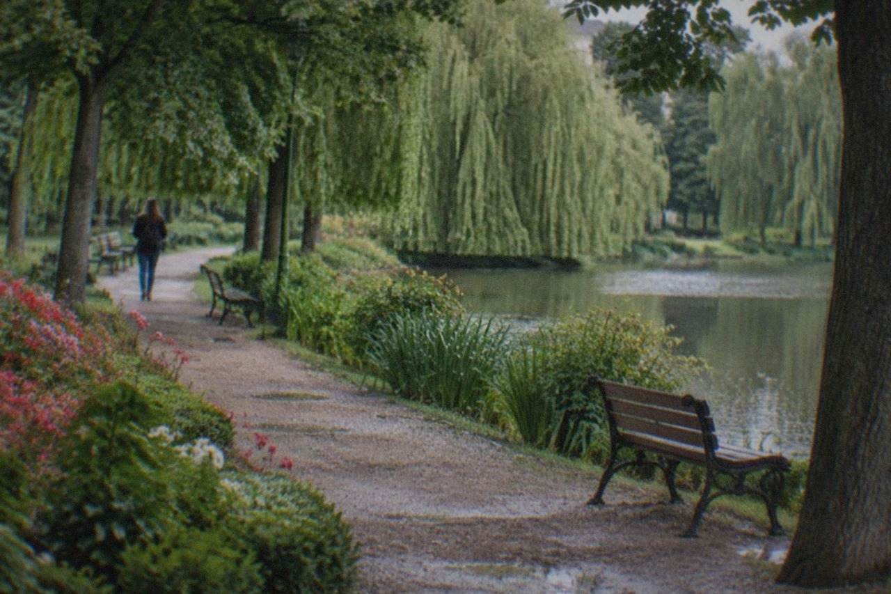 Tree-lined gravel path through a city botanical park with flowerbeds and benches