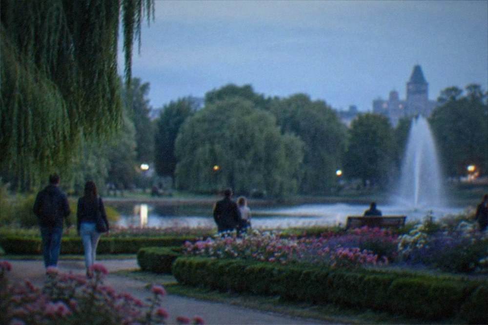 Visitors strolling beside flowerbeds and a fountain in a city park
