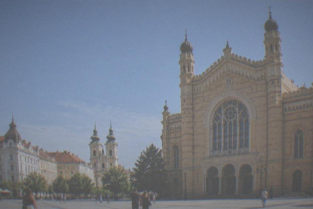 People strolling across a large square lined with baroque buildings and church towers
