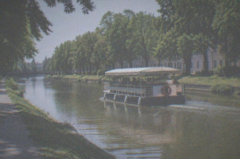 A passenger boat moving along the Bega canal between green banks in Timisoara