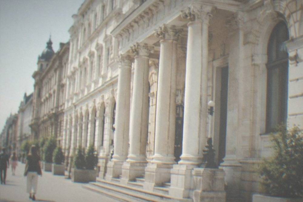 Pedestrians walking on a wide sidewalk past ornate historic facades on a sunny afternoon