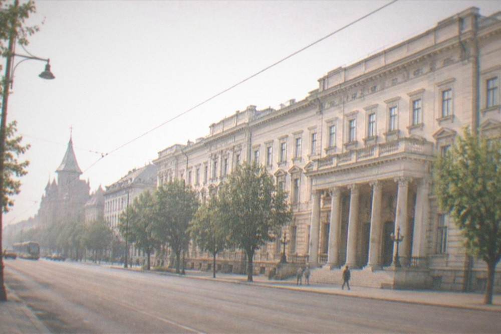 Wide view of a European city boulevard with historic buildings, tram tracks and green trees