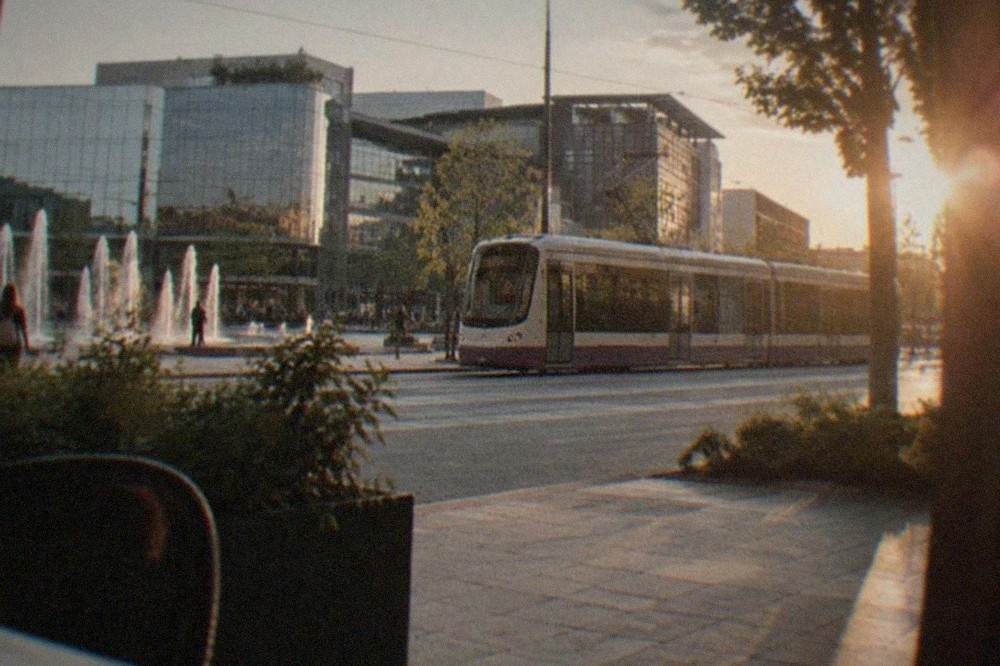 Modern tram passing a shopping complex entrance on a wide city boulevard