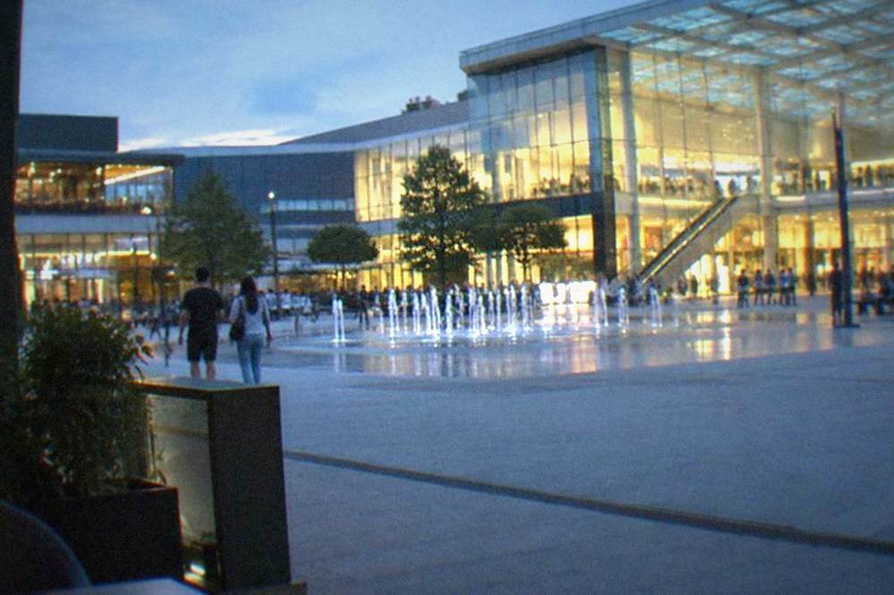 Bright shopping mall interior with upper walkways, escalators and storefronts under a glass roof