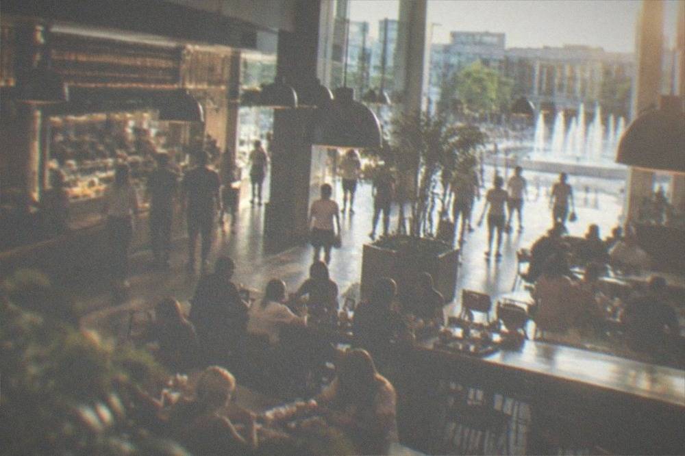 Busy food court with long shared tables, food counters and pendant lighting