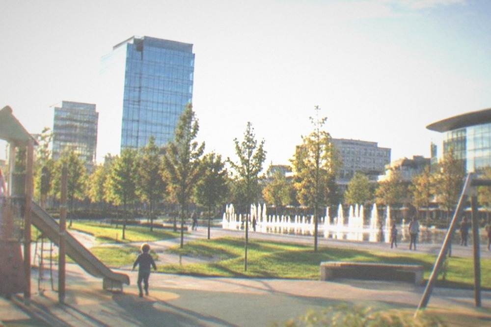 Children playing on a modern playground with lawns and office towers in the background