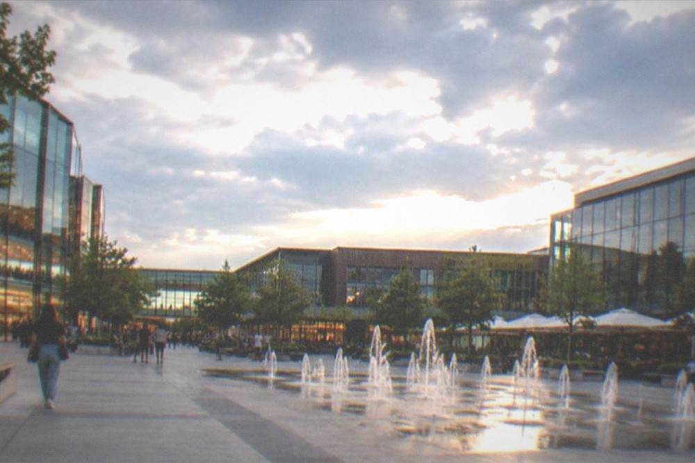 Shopping mall atrium lit for evening with illuminated storefronts and people on ground floor