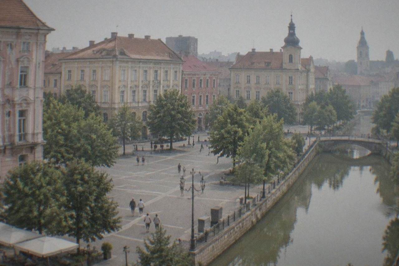 A quiet historic square in Timisoara with colorful facades, trees, and people walking across open paving