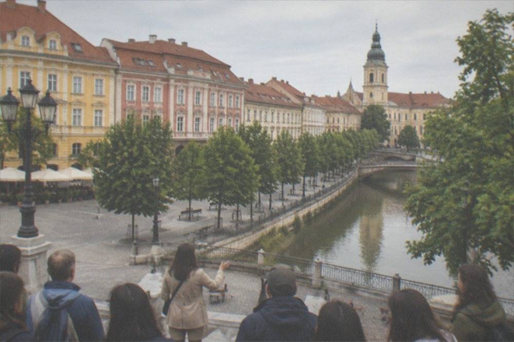 A walking tour group listening to a guide in a historic Timisoara square