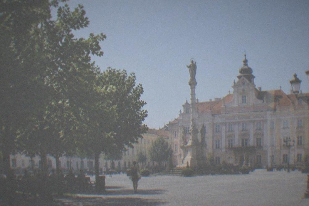 A European city square in summer with green trees and people sitting in the shade