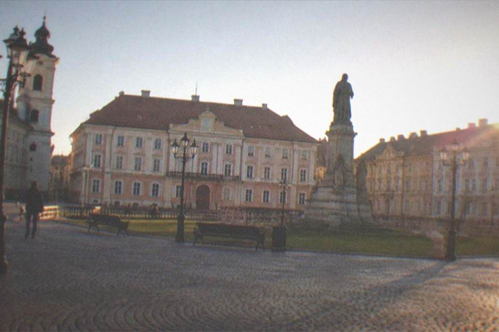 A wide view of a small historic square with ornate building facades and a clear sky