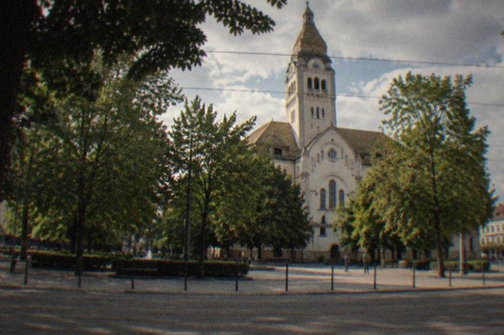A church facade seen across a tree-lined square with tram tracks in the foreground