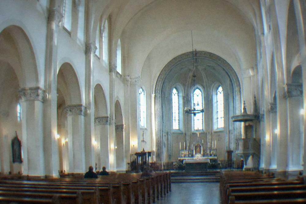 Interior of a spacious church with columns, arches and light falling on the nave