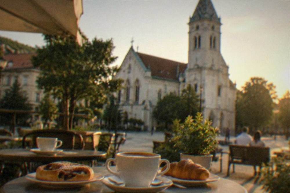 A cafe terrace with coffee cups and pastries on small tables in a city square