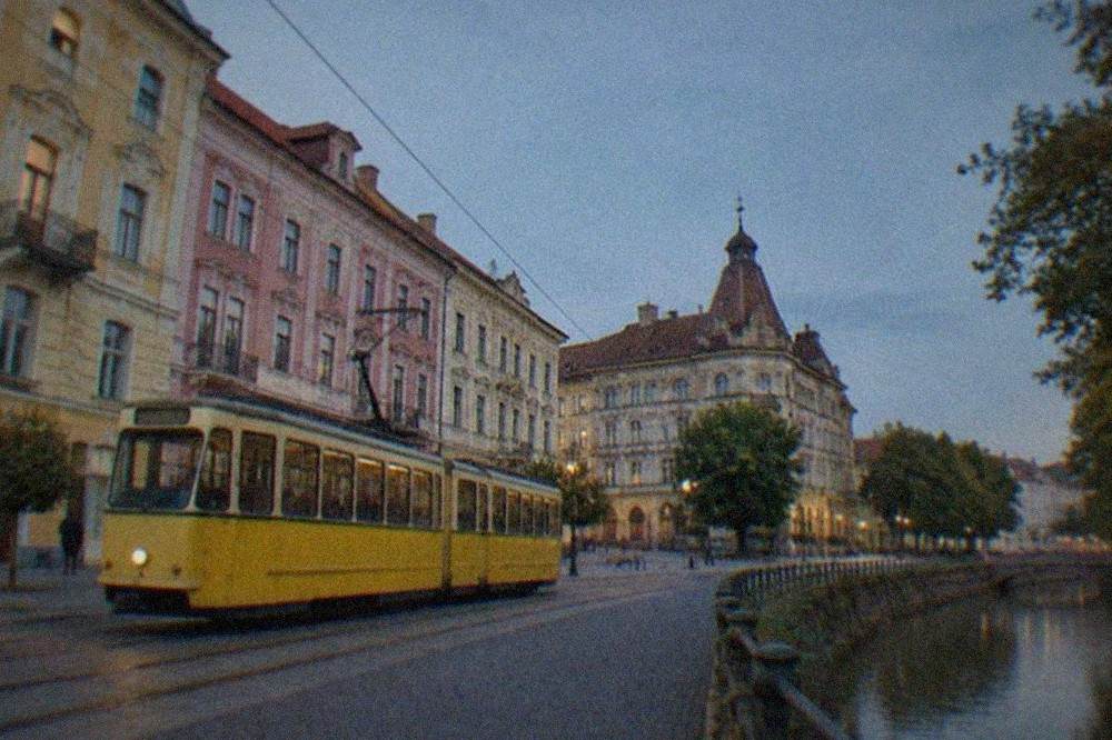 A restored yellow tram on tracks passing pastel colored buildings in Timisoara