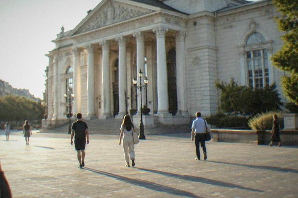 People walking across the open square in front of the Opera on a sunny afternoon