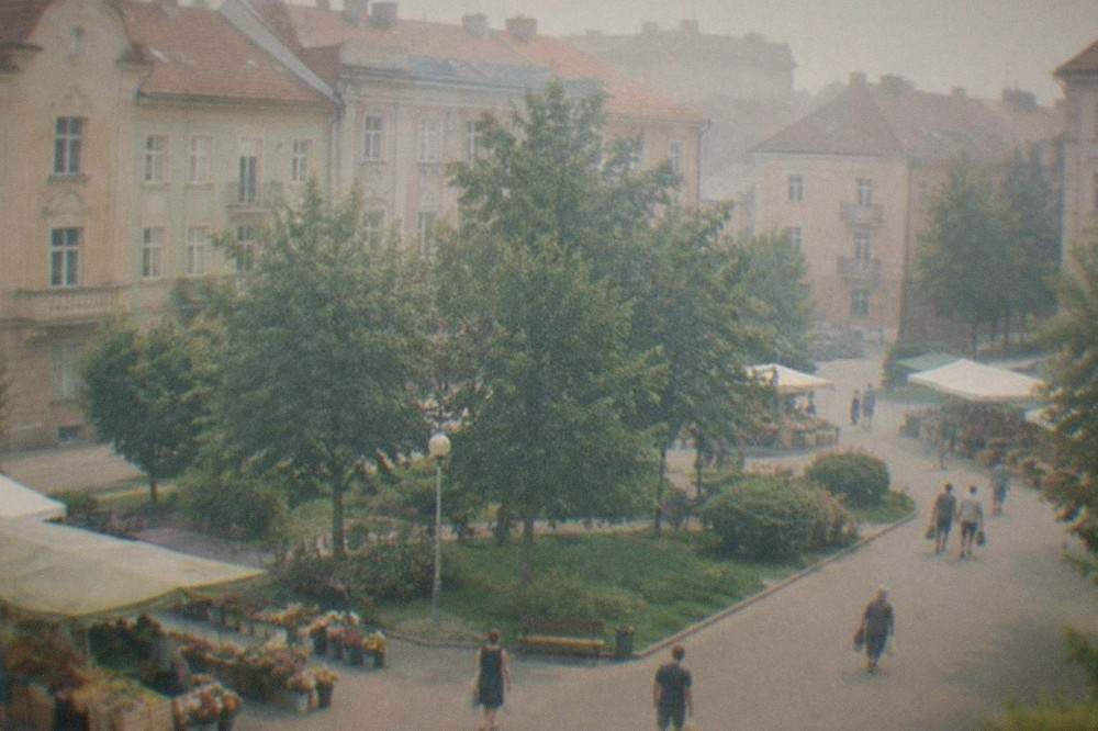 People walking past produce and flower stalls in a neighborhood market square