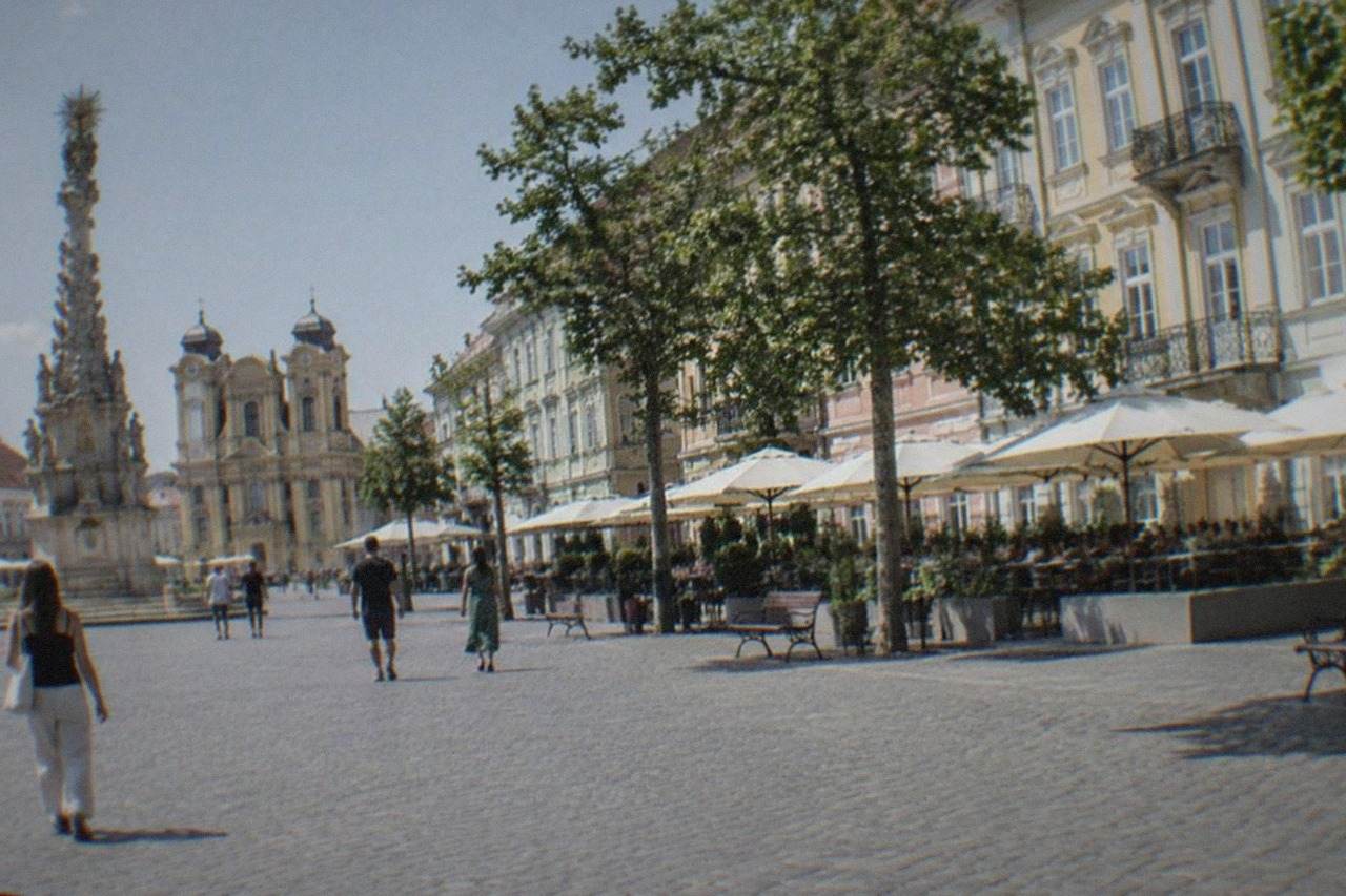 Baroque buildings and café terraces lining a wide city square on a sunny afternoon