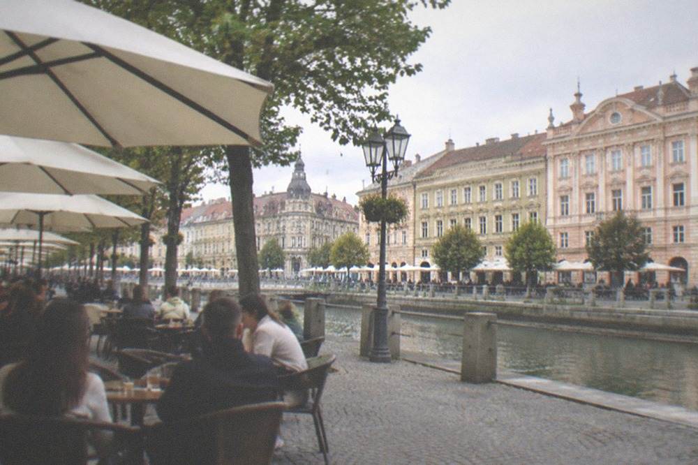 People seated at outdoor cafe tables under umbrellas beside a historic square
