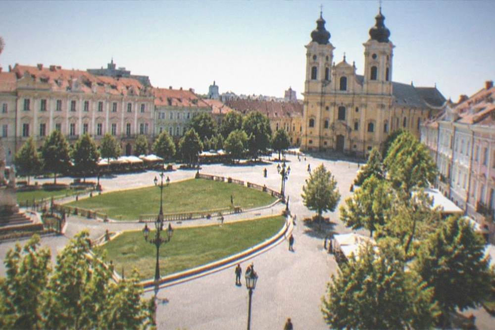Wide view of a Baroque city square with cathedral towers under a clear sky