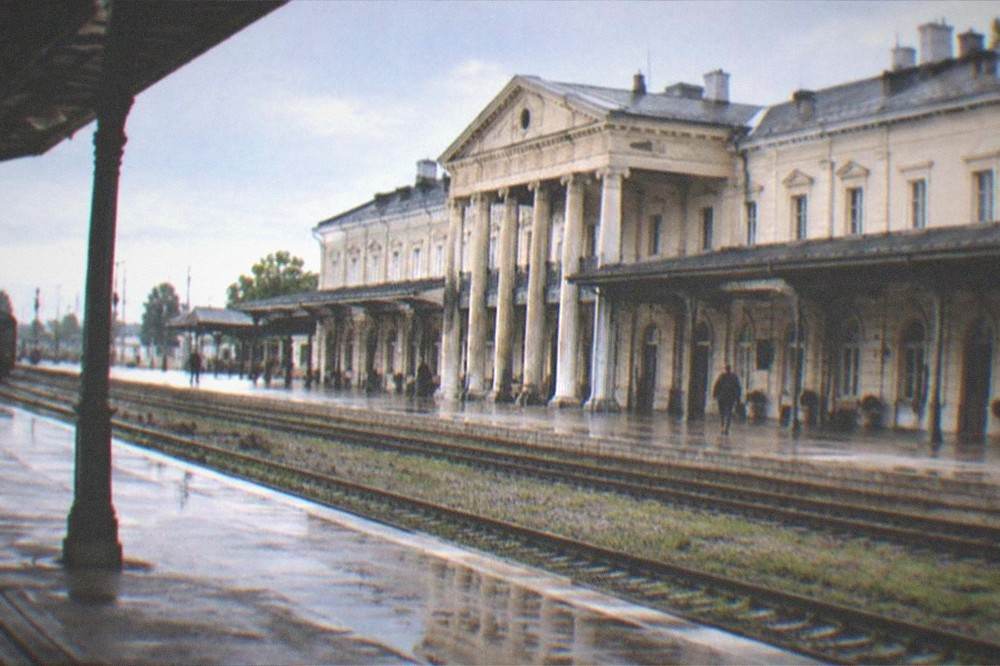 A steam-era railway station platform with old signage beneath wooded hills at dusk